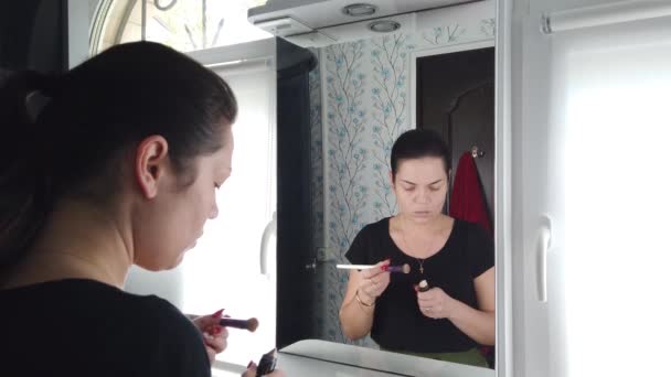 Mujer morena bonita haciendo maquillaje delante del espejo en el baño
 - Metraje, vídeo