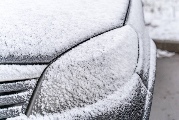 Zwarte auto koplamp bedekt door sneeuw in de winter. Auto in de sneeuw storm buiten - Foto, afbeelding