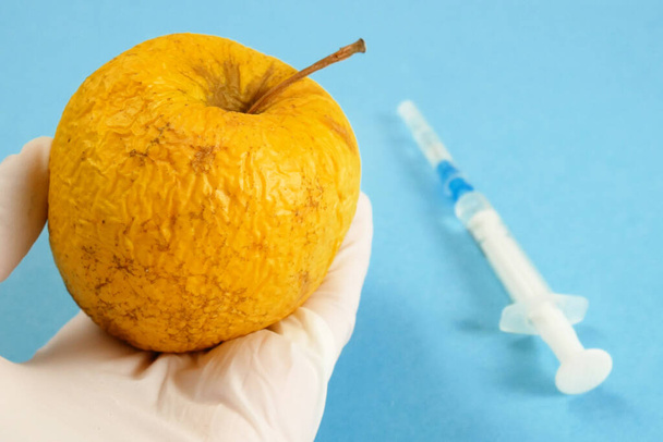 alma a géntechnológiai laboratóriumban fecskendővel és kémcsövekkel kék alapon, gmo food koncepció - Fotó, kép