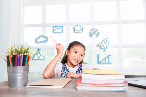 Holčička držící tužku s úsměvem s učebnicemi na stole s ikonami, e-learning on-line vzdělávání koncept - Fotografie, Obrázek