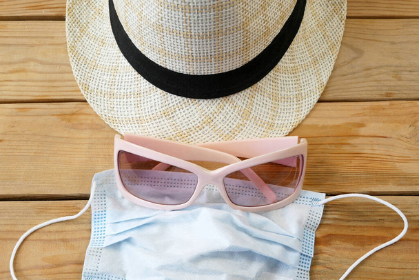 covid - 19, coronavirus concept, sun hat, sunglasses, sea shell, summer hat and medical mask on wooden background, flat lay, borders are closed, problems in the tourism business due to coronavirus - Photo, Image