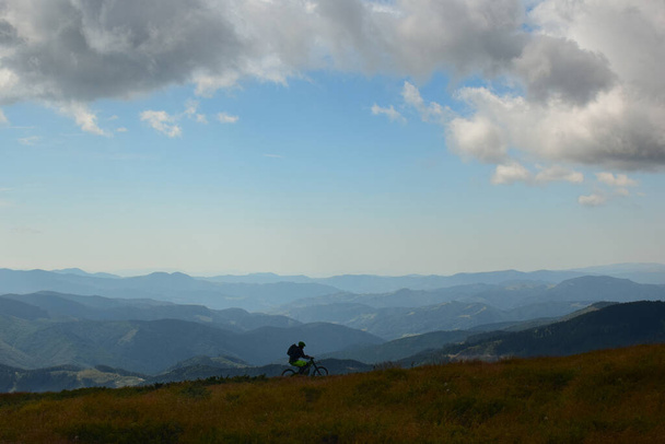 Самотній велосипедист їде на вершині гори влітку і на задньому плані віддалених гір
 - Фото, зображення