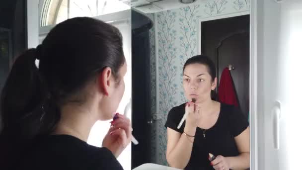 Όμορφη μελαχρινή γυναίκα κάνει μακιγιάζ μπροστά στον καθρέφτη στο μπάνιο - Πλάνα, βίντεο
