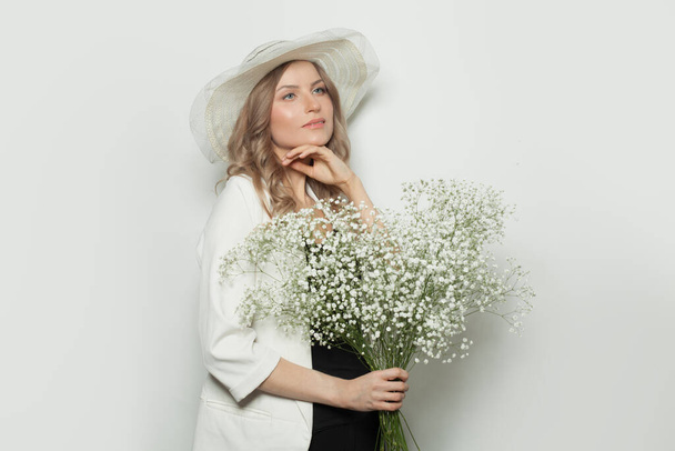 Atractiva mujer con sombrero de verano sosteniendo flores sobre fondo blanco
 - Foto, imagen