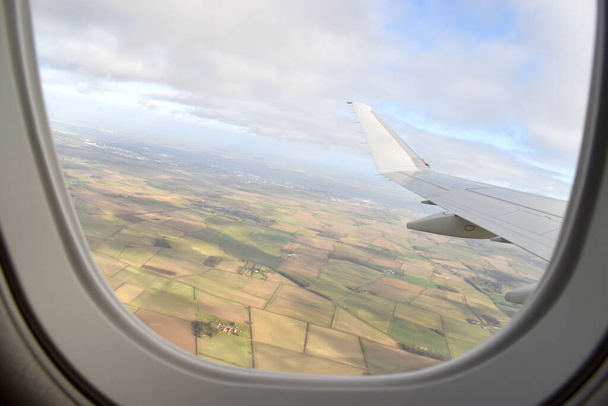 青い空に雲のある白い飛行機の翼の下の緑の土地の風景、飛行機の窓を通して見る. - 写真・画像