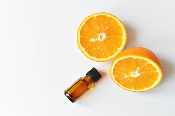 Orange citrus essential oil in dark glass bottle with fresh orange fruit halves. Aromatherapy treatment concept. Top view, copy space. - Photo, image