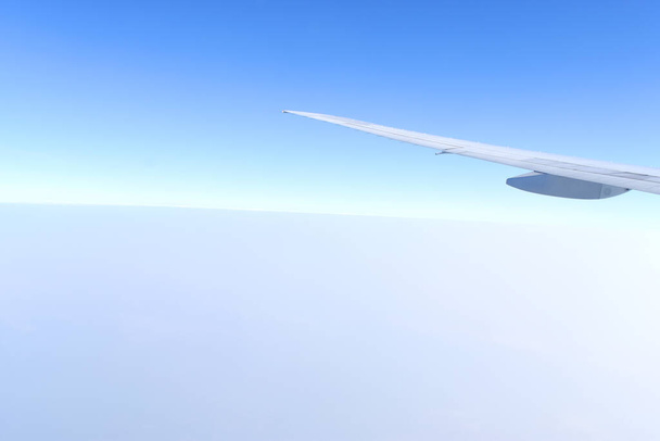 水平線の青い空と雲の上を飛行する飛行機の白い翼 - 写真・画像
