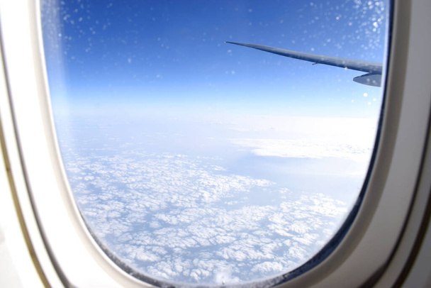 Смотреть сквозь окно самолета на облачность в голубом небе
 - Фото, изображение