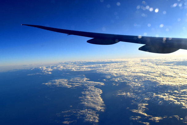 Силуэт крыла Airplan, летящего над облаками в горизонтальном голубом небе с солнечным светом, вид из окна самолета
. - Фото, изображение