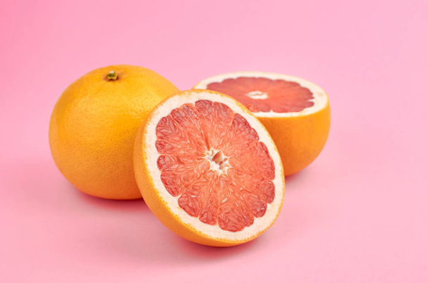 Fresh whole and cut grapefruit citrus fruits on trendy pink paper background - Valokuva, kuva