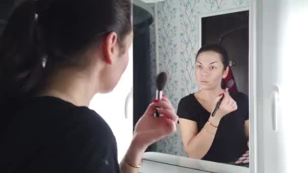 Kaunis brunette nainen tekee meikki edessä peili kylpyhuoneessa
 - Materiaali, video