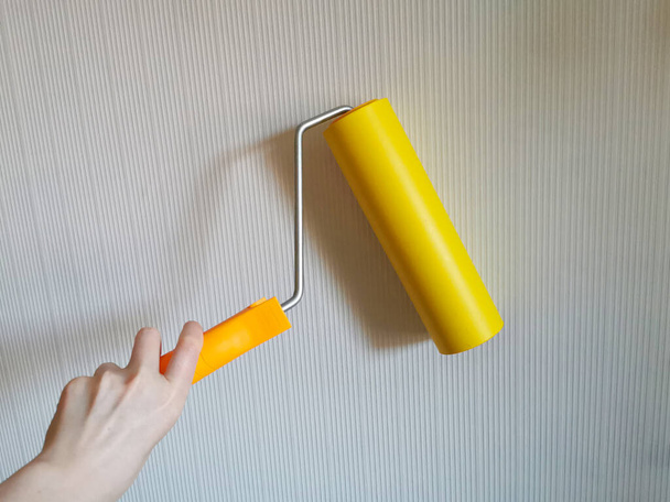 Werkzeug, Walze zum Glätten von Tapeten gelb. Farbroller mit rotem Griff und einer gelben, glatten Düse auf hellem Hintergrund. Tapezieren in der Wohnung. - Foto, Bild