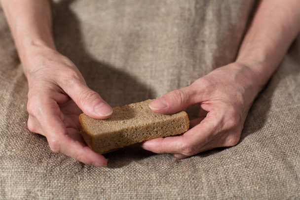 Senile hands hold a slice of rye bread. Close-up. - Foto, Bild