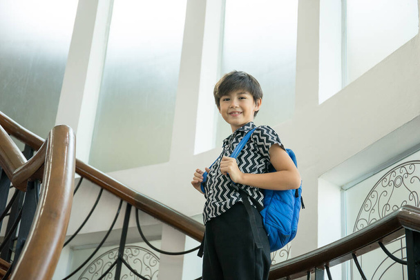 A fiú hátizsákkal a lépcsőn áll, miután visszajött az iskolából. - Fotó, kép