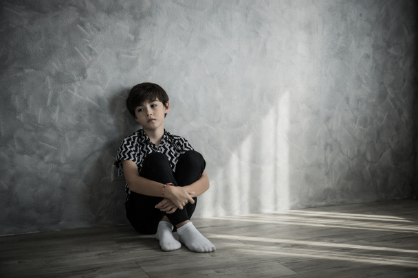 Niño triste sentado pensando sentado en el suelo de la habitación contra la pared de la casa
. - Foto, imagen