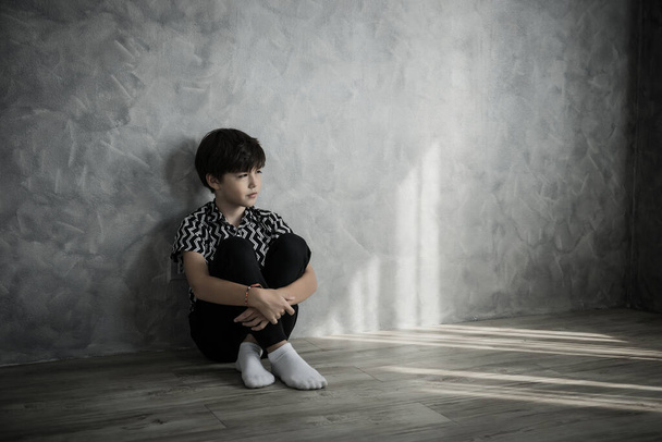 Szomorú fiú ül gondolkodás ül a padlón a szobában szemben a ház falán. - Fotó, kép