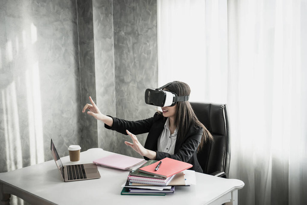 Деловая женщина в наушниках виртуальной реальности, указывая в воздух, сидя на своем рабочем месте
.  - Фото, изображение
