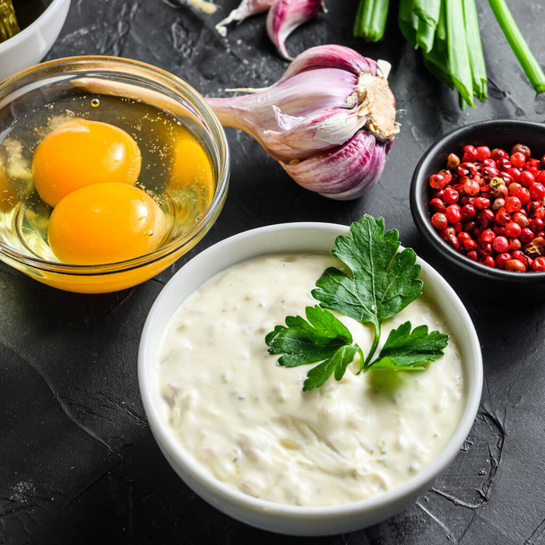 Organic lemon ranch dressing in a small jar with fresh greens. Tartar sauce. Making sauce from capers, cucumbers, parsley, lemon and eggs. For fish and chips and sea food Square on black stone surface. - Photo, Image