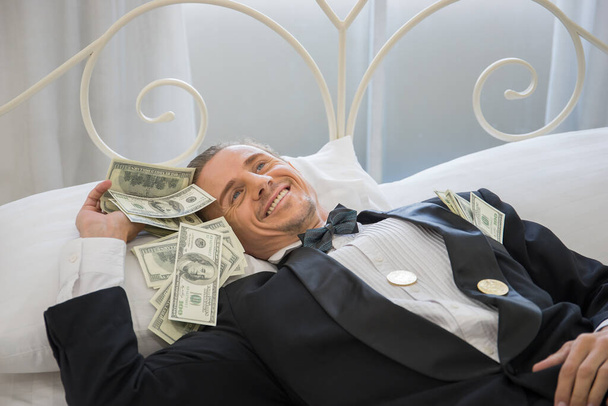 Богач лежит на кровати с долларовыми купюрами. Концепция успешного бизнеса
. - Фото, изображение