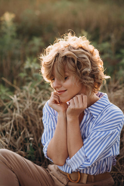 Menina bonita livre com cabelos cacheados coquettishly sorri em um campo com trigo ao pôr do sol. Foco seletivo suave
. - Foto, Imagem