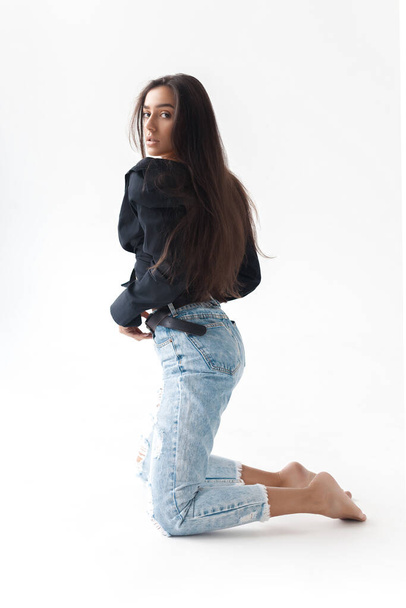Young cool hipster girl in black shirt and blue banana jeans kneeling on white background. Fashionable modern style - Fotografie, Obrázek