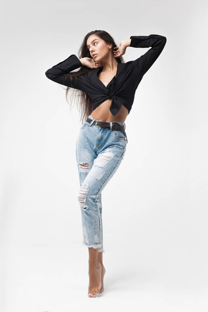 Young cool hipster girl in black shirt and blue banana jeans stands on white background. Fashionable modern style - Valokuva, kuva
