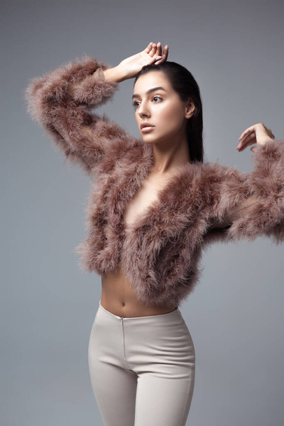 Young elegant girl posing in fluffy pink cape with artificial fur and beige flare trousers on gray background. Fashion retro style - Φωτογραφία, εικόνα