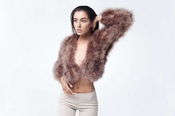 Young elegant girl posing in fluffy pink cape with artificial fur and beige flare trousers on gray background. Fashion retro style - Foto, Bild