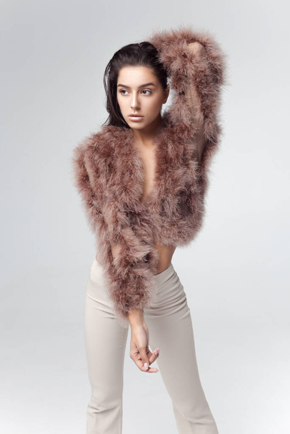 Young elegant girl posing in fluffy pink cape with artificial fur and beige flare trousers on gray background. Fashion retro style - Foto, Imagem