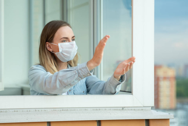 Woman applauds on the balcony of her apartment, thanking the medical services for Covid-19. - Fotoğraf, Görsel