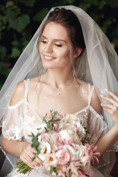 Brunette bride in fashion white wedding dress with makeup. Wedding day of bride in bridal gown. Beauty woman and bouquet. Fashion brunette model outdoors. Portrait beauty model in white bridal dress. - Foto, Imagen