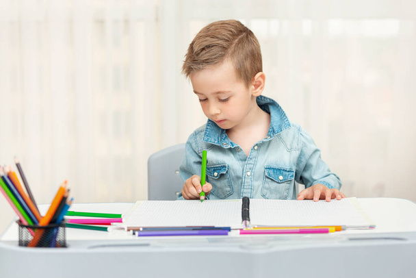 Küçük çocuk ödevlerini yazıyor ve resim yapıyor. Anaokulu öğrencisi yazmayı ve çizmeyi öğrendi..  - Fotoğraf, Görsel