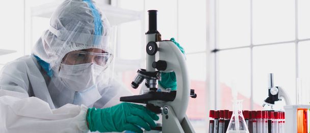 banner picture of scientist in personal protective equipment or ppe doing research and experiment to find drugs to treat covid-19 or coronavirus infection in the lab - Photo, Image