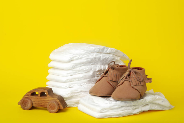 Diapers, toy car and baby shoes on yellow background - Photo, image