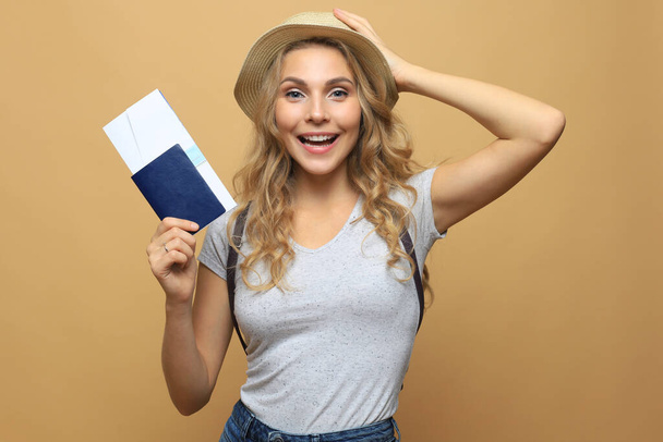 Mooie blonde vrouw in de zomer kleding poseren met paspoort met tickets over beige achtergrond - Foto, afbeelding