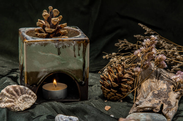Beauty composition with Burning candle aroma oil lamp and Dry flower petals and Pine cones, Natural pine wood disc, Stones and Shells, Himalayan salt on dark background. Aromatherapy concept. - Photo, Image