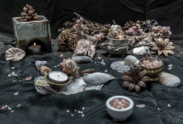 Beauty composition with Burning candle aroma oil lamp and Dry flower petals and Pine cones, Natural pine wood disc, Stones and Shells, Himalayan salt on dark background. Aromatherapy concept. - Photo, Image