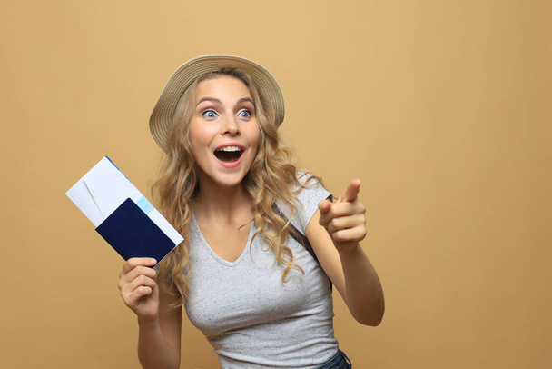 Hermosa mujer rubia con ropa de verano posando con pasaporte con entradas sobre fondo beige
 - Foto, Imagen