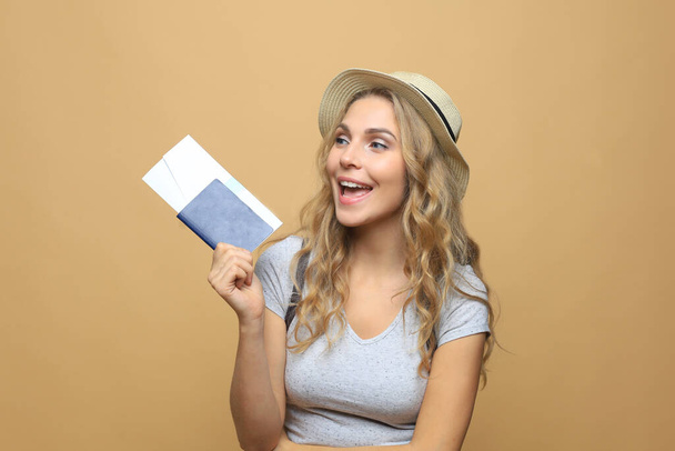 Beautiful blonde woman wearing summer clothes posing with passport with tickets over beige background - Fotografie, Obrázek