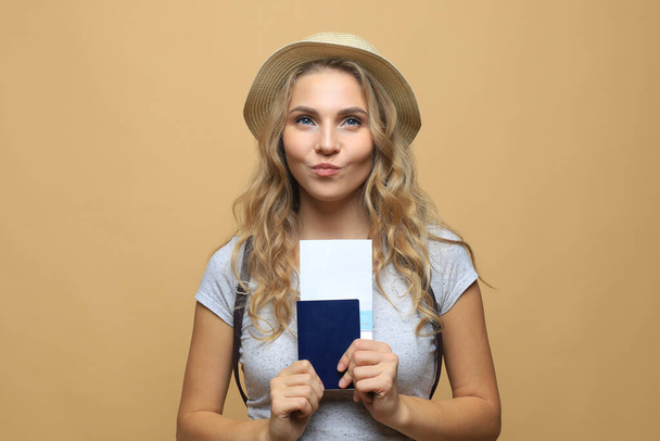 Beautiful blonde woman wearing summer clothes posing with passport with tickets over beige background - Zdjęcie, obraz