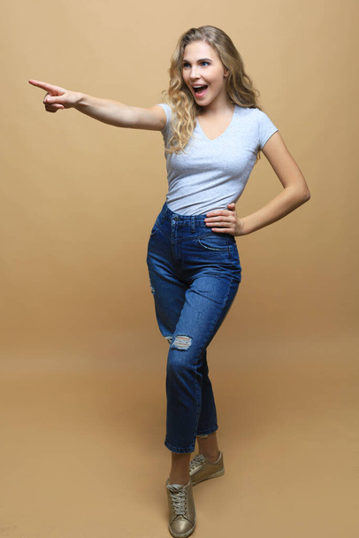 Image of happy young woman standing isolated over beige wall background. Looking camera showing copyspace pointing - Fotografie, Obrázek