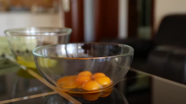 Yemas de huevo separadas en un recipiente transparente de vidrio en primer plano, en el fondo claras de huevo, en una mesa de vidrio negro en la cocina del hogar
. - Metraje, vídeo