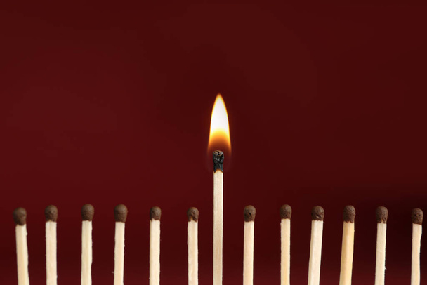 Burning match among unlit ones on red background, closeup - Photo, Image