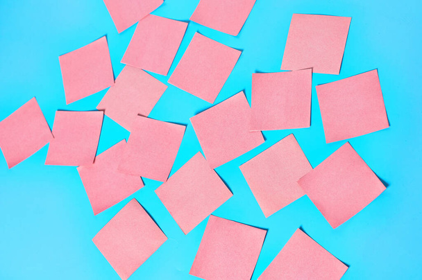 Scattered many pink square blank paper stickers on blue background - Fotografie, Obrázek