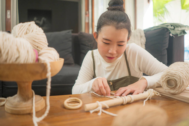 Asian girl enjoying macrame handcraft hobby - young happy and pretty Japanese at home doing macrame using ropes, cords and threads in domestic handmade decoration - Foto, imagen
