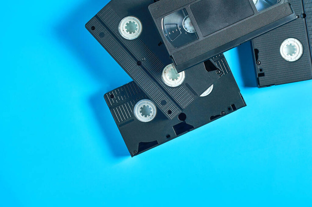 Heap of black old plastic vhs video cassettes lies on blue desk. Concept of 90s. Copy space. Top view - Zdjęcie, obraz