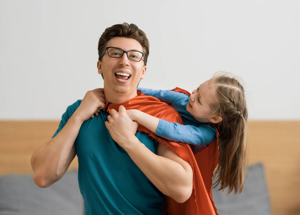Father and his child playing together. Girl and dad in Superhero costume. Daddy and kid having fun, smiling and hugging. Family holiday and togetherness. - Fotoğraf, Görsel