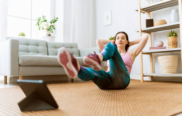 Young woman in activewear watching online courses on tablet while exercising at home. - Φωτογραφία, εικόνα