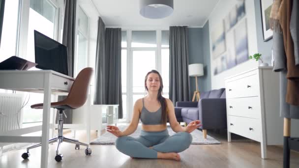 Žena sedí v lotosové pozici a medituje uprostřed místnosti doma - Záběry, video