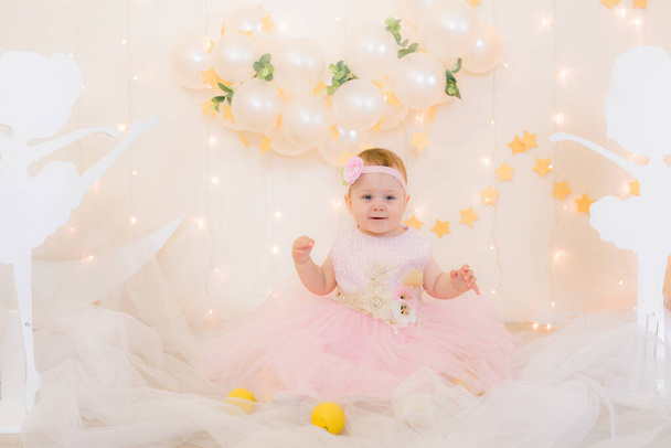 Cute little girl in a pink princess dress with a flower on her hair plays with wooden ballerinas among the golden stars on the background of a large white wooden moon and balloons. Children's decor.  - Photo, Image